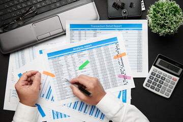 Top view of businessman's hands working with financial reports. Modern black office desk with laptop, notebook, pencil and a lot of things. Flat lay table layout.