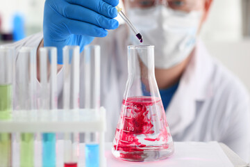 A male chemist holds test tube of glass in his hand overflows a liquid solution of potassium permanganate conducts an analysis of water samples versions of reagents using chemical manufacturing