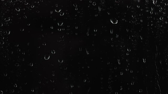 4K footage of rain drops falling on window glass on black background.