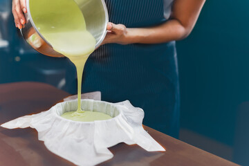 Woman pouring matcha green tea dough into a mold padded with parchment paper.