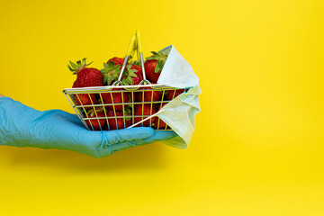 shopping basket with strawberries in a medical mask on a yellow background