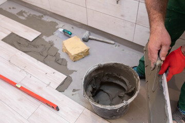 The builder applies cement adhesive to the ceramic tile with a stainless trowel.
