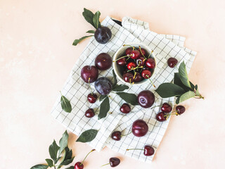 Summer fruits on pink texture table. Plum, cherry and green leaves. Copy space, Top view
