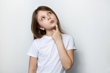 A beautiful healthy little girl in white clothes on a white background thinks and looks up dreamily. Copy space for text