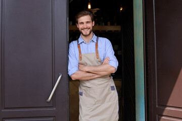 Handsome and confident cafe owner standing at the door. Young man standing with his arms crossed...