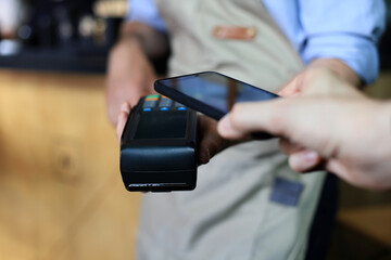 Customer using smartphone for payment to owner at cafe restaurant, cashless technology.