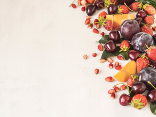Various berries and fruits on a white background. Border of strawberries, wild strawberies, cherries, peach, plum. Copy space