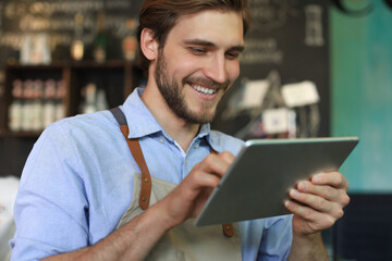 Young male owner using digital tablet while standing in cafe.