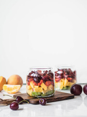 Two glass jars with berries and fruits. Fruit salad with kiwi, peach, strawberry, cherries and plum in glass jars on wood board. Summer seasonal tasty vegetarian salad for a snack or lunch