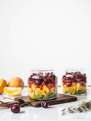 Two glass jars with berries and fruits. Fruit salad with kiwi, peach, strawberry, cherries and plum in glass jars on wood board. Summer seasonal tasty vegetarian salad for a snack or lunch