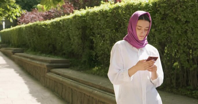 Beautiful young woman looking at smartphone, wearing traditional headscarf. Attractive Female in hijab