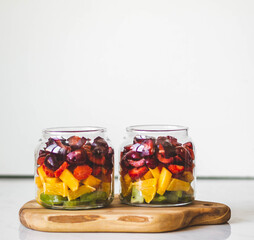 Fototapeta na wymiar Two glass jars with berries and fruits. Fruit salad with kiwi, peach, strawberry, cherries and plum in glass jars on wood board. Summer seasonal tasty vegetarian salad for a snack or lunch