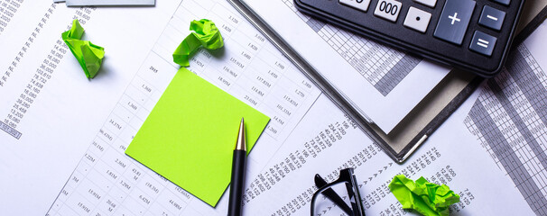 On the working table are a calculator, stickers, glasses, pen and money. Top view close up business concept