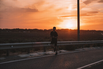 Attractive fit man running along modern bridge at sunset light,