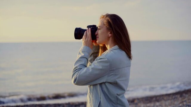 Young casual woman photographer takes pictures of the sea using a professional camera dslr