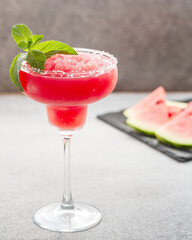 Watermelon margarita cocktail with lime. Watermelon summer cocktail with ice and mint leaves. Cold refreshment drink in a glass with water drops. Low depth of field, selective focus.