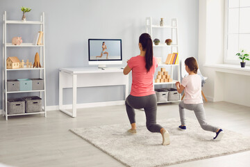 Family does exercises online. Mother and daughter watch online fitness trainer video course in room...