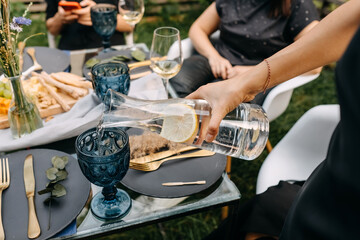 Female hand pouring still water with lemon in a glass at a party.