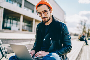 Portrait of skilled man dressed in stylish outfit sitting outdoors with modern netbook, caucasian...
