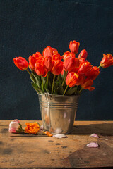 bouquet of red tulips in a metal bucket on a wooden table on a dark background