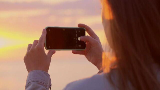 Woman traveler taking picture of the sea at sunset on the smartphone camera 