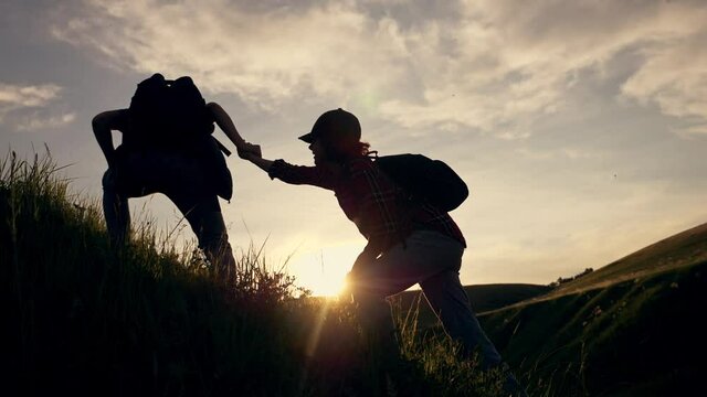 Teamwork. Travelers lend a helping hand, overcoming obstacles, climbing to the top. Business, the path to success. Silhouette of tourists at sunset in the mountains in the sun.