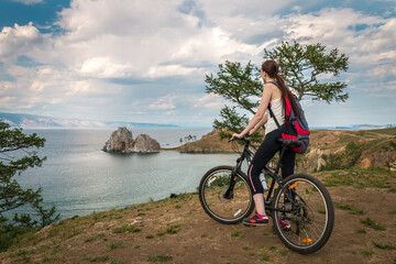 Fototapeta premium a girl travels on a bicycle with a backpack on Lake Baikal