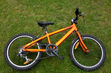 Fototapeta na wymiar An orange children's Bicycle is lying on the green grass