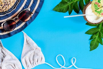 Striped hat, sun glasses, palm leaves, .white swimsuit, coconut half with milk cocktail are laid out on blue background. Tourism, tours to foreign exotic tropical countries concept. Vacation mood.