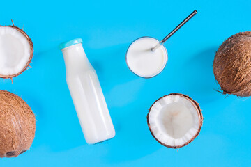 Coconut based foods are scattered on blue background. Alternative white milk in glass with straw, bottle, nut halves are on table. Natural healthy organic vegan vegetarian meal concept.