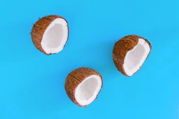 Brown halves of coconut nuts are stacked in triangle on blue background. Tropical palm fruit....