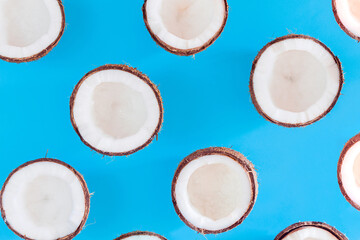 Brown halves of coconut nuts are scattered on blue background. Tropical palm fruit. Organic natural healthy vegan vegetarian meal, coco based food concept. Exotic pattern, backdrop, wallpaper.