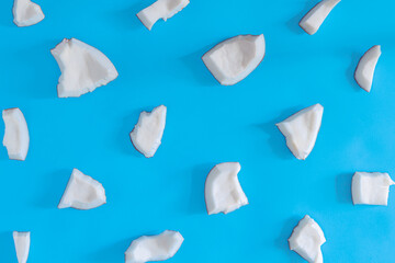 White shavings, pieces of coconut nuts are scattered on blue background. Tropical palm fruit. Organic natural healthy vegan vegetarian meal, coco based food concept. Exotic pattern, backdrop.