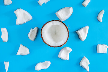 Brown half of coconut nut on blue background. Shavings, white pieces are scattered around. Tropical...