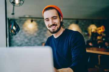 Portrait of cheerful caucasian man in trendy bennie satisfied with online language courses using...