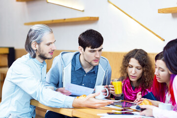 Young people guys and girls are having meeting, sitting at table in cafe. Creative colleagues, students are discussing project, business strategy, documents with diagrams. Team work concept.