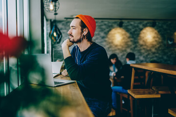 Contemplative hipster guy dressed in stylish apparel thoughtful looking away while listening...