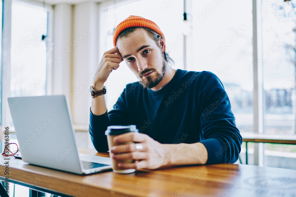 Poster portrait of caucasian male freelancer in trendy apparel sitting at cafeteria table and doing remote 