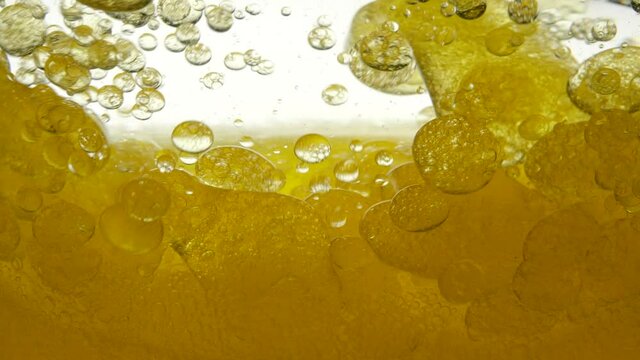 Close-up view of golden liquid in a glass. Liquid yellow wave line. Middle view of large and small air bubbles on a white background. Gold-colored liquid in a container. Sunflower oil mixes with water