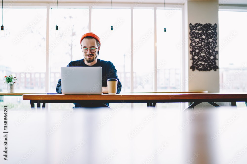 Poster skilled positive hipster guy satisfied with wifi connection for e learning in coffee shop using lapt