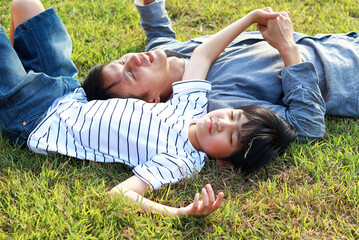 Asian father and son lie happily on the grass in the park. The concept of love, attachment of father and child