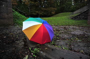 Rainbow colored umbrella in park area.  The umbrella is placed in a circle of flat stones. Artillery battery from World War 2 visible.