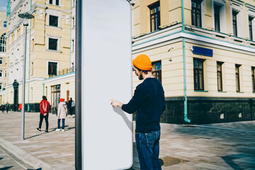 Back view of Caucasian male traveler searching information on touristic billboard pointing on white...