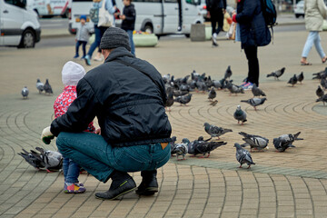 A father and his daughter feed pigeons on a street