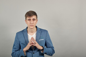 Thinking over problem trying to focus at work, holding hands in concentration gesture collecting thoughts or making important decision. Young attractive man, dressed blue jacket, grey background