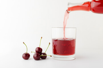 Process of pouring cherry drink into glass and heap of cherry on the white background