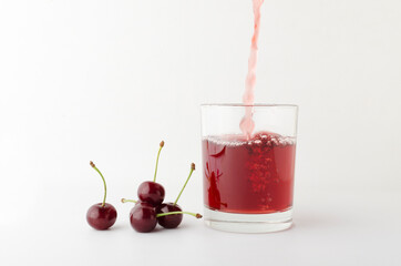 Pouring fresh and sweet cherry drink into the glass, heap of cherries on the white background