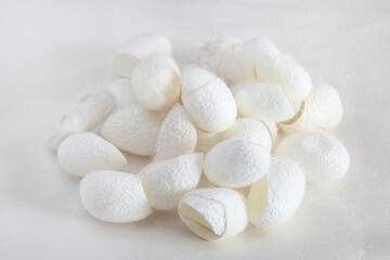 Fototapeta na wymiar many organic silkworm cocoons for facial skin care on white silk fabric