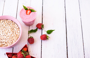 Fresh strawberry yogurt with berries around on a white wooden background. A pink shake in a glass, next to it is a pink cup with Hercules flakes, and red strawberries lie in a red star-shaped plate