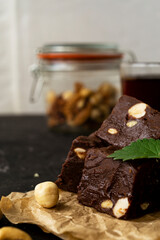 Fondant on craft crumpled paper with nuts and chocolate cubes decorated with green mint leaves. In the background a jar of nuts, blurred background. Sweet composition on a black textural background. 